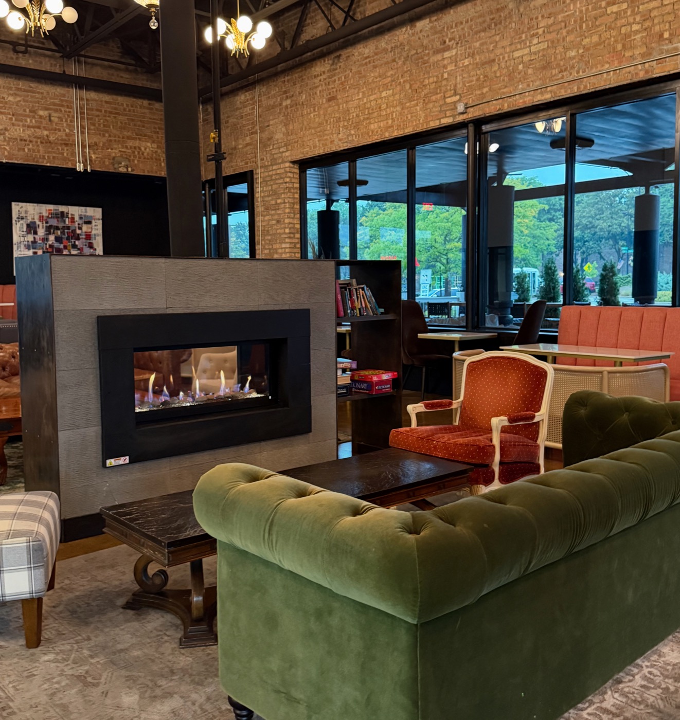 The lit double-sided fireplace beside a green velvet chesterfield sofa and a vintage red armchair